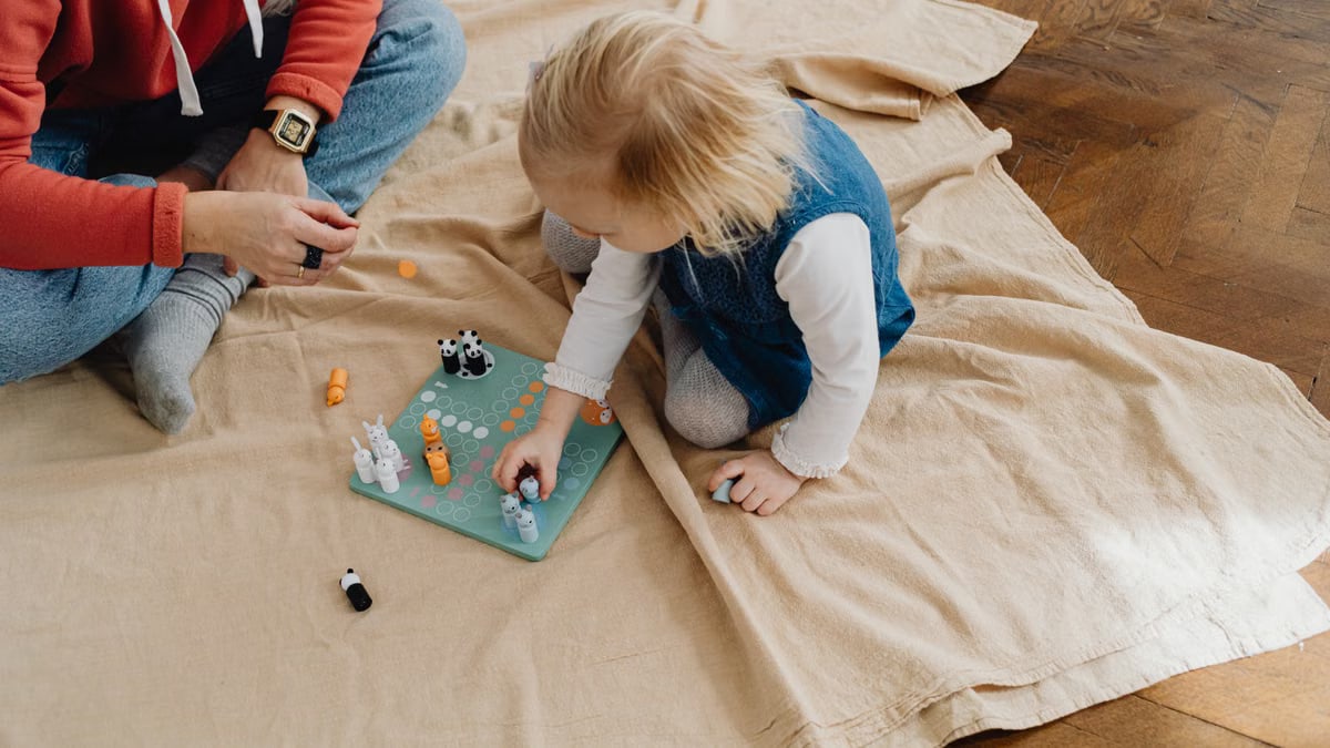 Child playing a board game with an adult on a wooden floor, enjoying indoor activities.